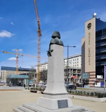 The Emperor Napoleon I Memorial bust on a tall plinth in a gravel plaza, with construction cranes and buildings in the background.