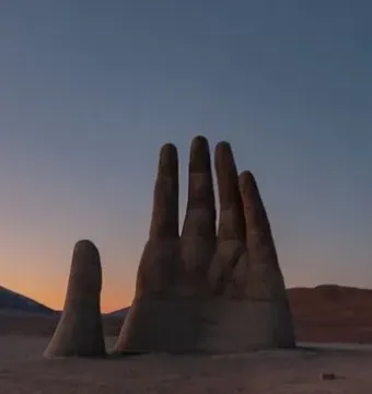 Mano del Desierto rising from a barren desert landscape at dusk with distant mountains on the horizon.