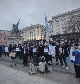Manuel Belgrano equestrian monument on a tall stone pedestal behind a crowd in Plaza de Mayo, with Argentine flags and the pink Casa Rosada in the background.