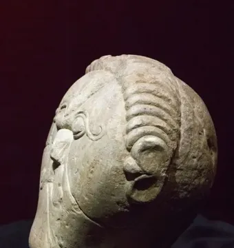 Mšecké Žehrovice Head stone sculpture shown in profile on a black stand, with stylized facial features and ribbed hair bands.