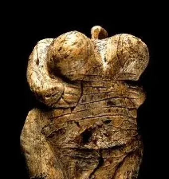 Venus of Hohle Fels figurine with pronounced breasts, rounded abdomen, and a loop-like top against a dark background.