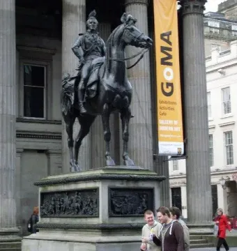 The Duke of Wellington equestrian statue with a traffic cone on its head, standing before a columned building with a GoMA banner.