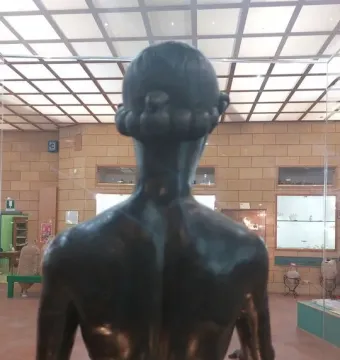 Back view of the Efebo de Selinunte bronze statue behind glass in a museum display.