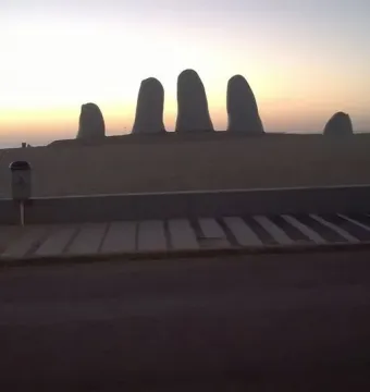The Hand sculpture rising from a sandy beach at sunset, with the ocean in the background.