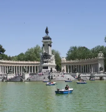 The Alfonso XII Monument with a central equestrian statue, flanked by curved colonnades beside a lake with rowboats.