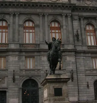 El Caballito, a dark equestrian statue on a stone pedestal, with a grand stone building in the background.