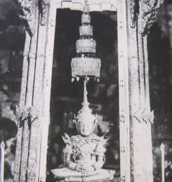 Emerald Buddha statue seated in meditation beneath an ornate shrine and hanging ornament.