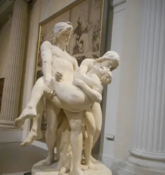The First Funeral marble sculpture showing three figures, with two adults carrying a limp smaller figure between them.