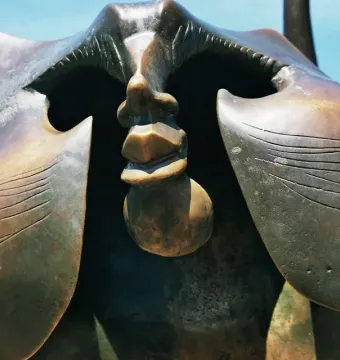 Close-up of the Heidelberg Bridge Monkey sculpture showing its hollowed face and stylized lips against the sky.