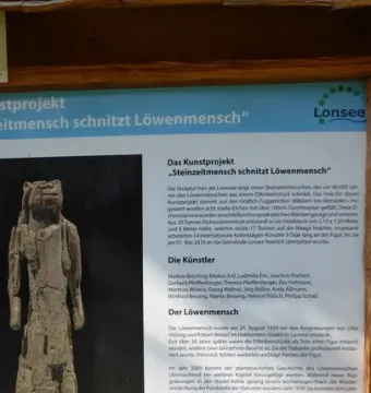 The Lion-man sculpture, a tall light-colored wooden figure with a human body and animal-like head beside an information board.