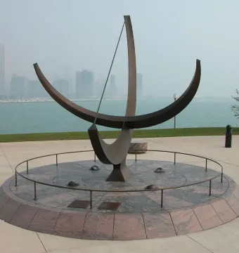 Man Enters the Cosmos sundial sculpture on a circular granite base with Chicago skyline and boats in the background.