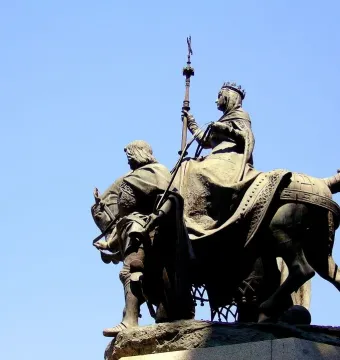 Monument to Isabella of Castile with a crowned woman on horseback and a bearded man beside the horse against a blue sky.