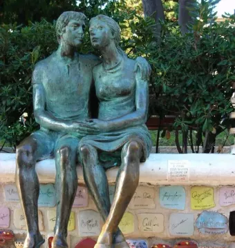 The Muretto of Alassio bronze sculpture of a seated man and woman embracing on a decorated stone wall