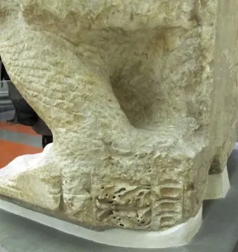 Lower section of the Palestrina Pietà in light marble, showing rough unfinished surfaces and chisel marks on a museum display platform.