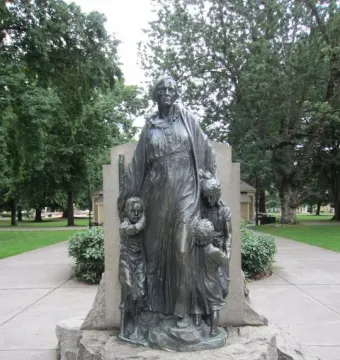 Pioneer Mother Memorial sculpture showing a standing figure with three children on a rocky base in a park setting.