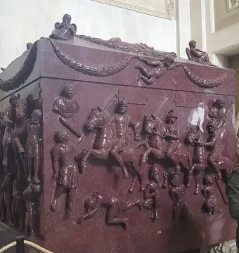 Sarcophagus of Helena with high-relief battle scenes of horsemen and foot soldiers in a museum gallery.