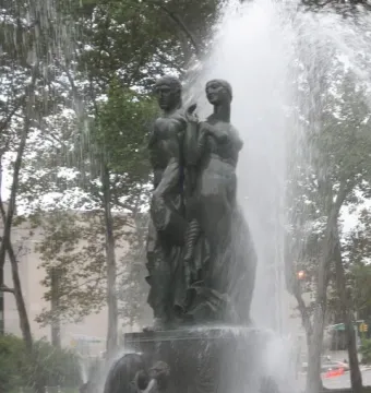 Bailey Fountain with a dark metallic man and woman standing back to back on a stone pedestal amid water sprays.