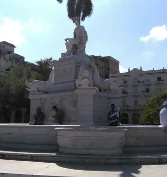 Fuente de la India marble fountain with a crowned female statue and fish sculptures at the base in a sunny plaza