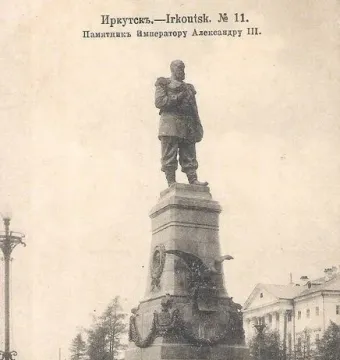 Monument of Alexander III on an ornate pedestal with a decorative iron fence in front of a classical building.