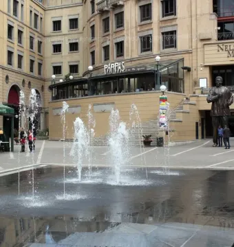 Nelson Mandela statue standing at the entrance of Nelson Mandela Square with fountains and people nearby.