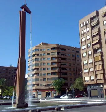 The Pink Panther sculpture fountain in a concrete plaza with apartment buildings and parked cars nearby.