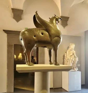 Bronze Pisa Griffin statue on a pedestal in a museum gallery.