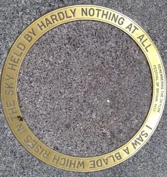 Circular brass commemorative plaque for the Skylon embedded in grey pebbled ground.