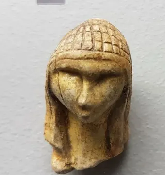 Replica of the Venus of Brassempouy showing a small stylized human head with a prominent nose and patterned hair or headdress.