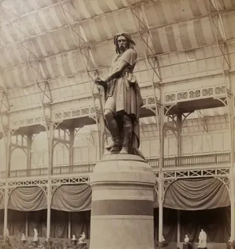 The Vercingetorix monument stands on a stepped circular pedestal inside a large glass-roofed exhibition hall.