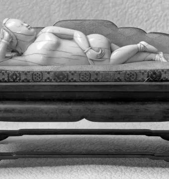 Doctor\'s Lady, a light-colored female figure reclining on a small couch with a patterned cushion, shown on a wooden stand.