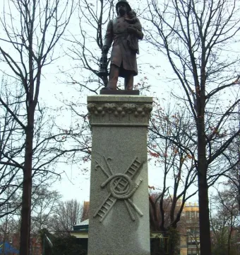 Firemen\'s Monument showing a bronze rescue worker holding a child and lantern atop a tall granite pillar.
