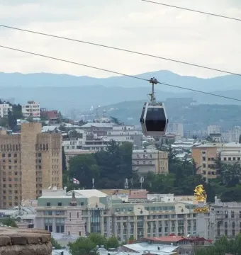 Freedom Monument rises above the Tbilisi skyline beneath gondola lift cables.