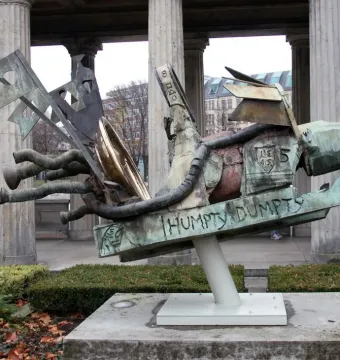 The Humpty-Dumpty Machine sculpture, a weathered bronze abstract form with green patina and gold accents on a white pedestal.