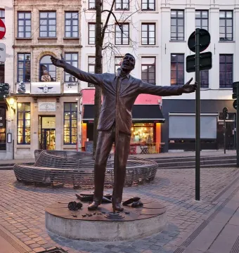 The Jacques Brel memorial bronze statue stands on a circular platform in a cobblestone square, with outstretched arms and a microphone stand nearby.