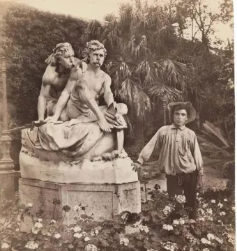 Kanaris brothers monument with two classical male figures in a garden, with a young man standing beside it