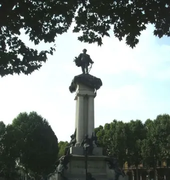 Monument to Vittorio Emanuele II topped by a statue on a tall column, with trees and a flower bed around the base.