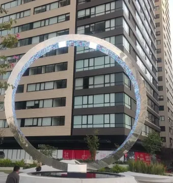 The Eye of Mexico sculpture in an urban plaza beside a tall gridded building, framed by trees and city streets.