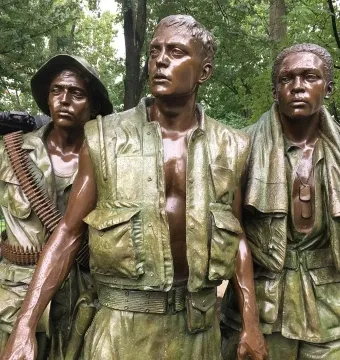 The Three Soldiers bronze statue with three wet-looking soldiers standing outdoors among trees.