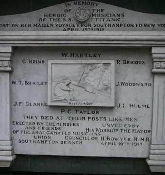 Titanic Musicians\' Memorial stone plaque mounted on a brick wall with inscriptions and a central relief carving.
