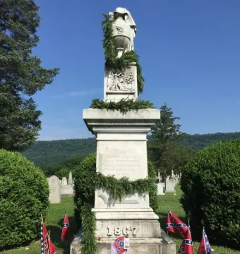 Confederate Memorial stone monument with an urn on top, garlands, and small Confederate flags around the base.