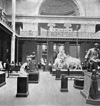 Dickens and Little Nell sculpture with a seated man resting his chin on his hand beside a young girl in a large exhibition hall.