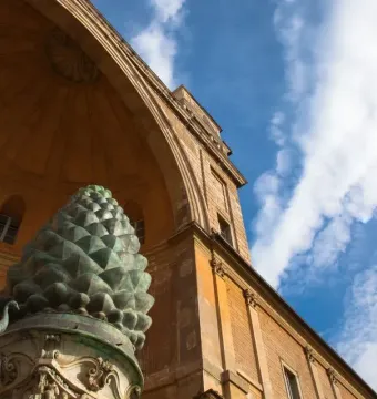 La Pigna bronze pine cone sculpture with a peacock beside it in a courtyard