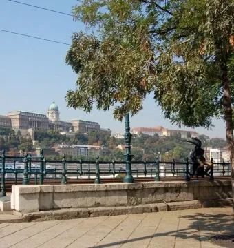 Little Princess statue sitting on a railing with a river and cityscape in the background.