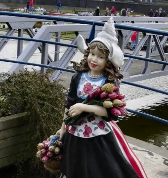 Madurodam statue of a Dutch girl in traditional dress holding tulips and wearing clogs beside the water.