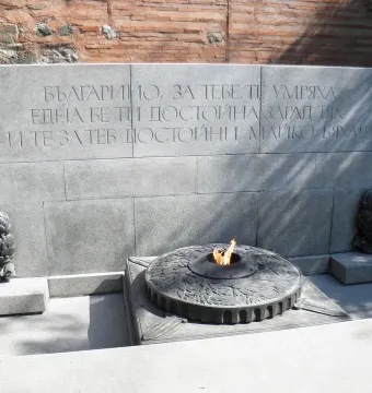 The Unknown Soldier Monument with a grey stone wall, Cyrillic inscription, and an eternal flame in a dark metal basin.