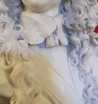 Close-up of the Bust of Francesco I d\'Este showing the marble curls, cravat, and draped clothing against a red background.