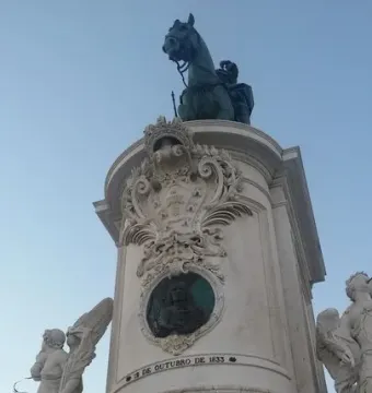Equestrian Statue of Joseph I on a tall ornate pedestal with marble figures and reliefs against a blue sky.