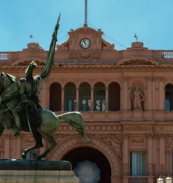 Manuel Belgrano equestrian monument in front of a pink building with arched windows and a central clock.