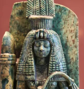 Weathered bust of Queen Tiye with an ornate headdress and heavy wig, shown in close-up.