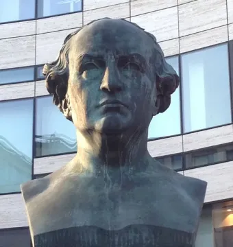 Schadow Monument bronze bust on a stone base with a modern building in the background.